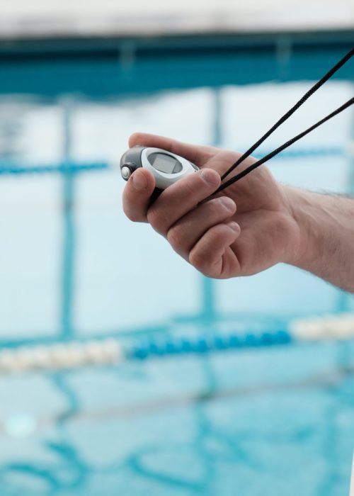 Close-up of unrecognizable coach with whistle using stopwatch while determining athletes performance in swimming pool