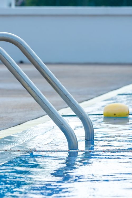 Ladder stainless handrails for descent into swimming pool. Swimming pool with handrail . Ladder of a swimming pool. Horizontal shot. stairs swimming pool. Stainless steel ladder
